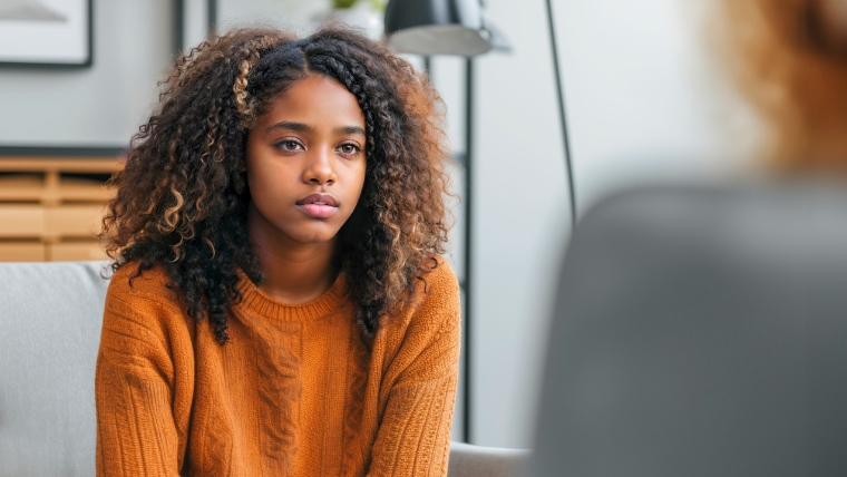 Teen girl sitting on a couch in a psychiatrist office looking sad and serious | How a Psychiatrist Helps Identify and Treat Adolescent Depression | Mindful Health Solutions