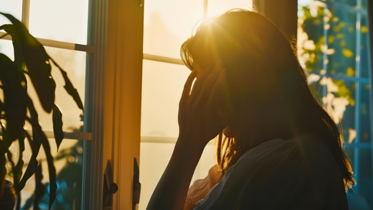 A woman's silhouette standing in front of a window with her hand to her head | 5 Reasons Why Depression Screening Is Now Recommended for All Adults | Mindful Health Solutions