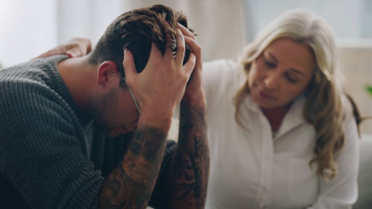 A man with his head in his hands being supported by a woman | How To Help Someone Calm an Anxiety Attack 