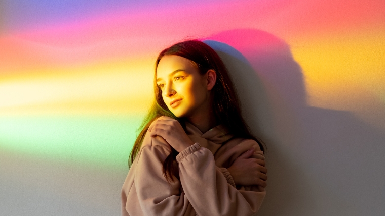 Young woman standing in rainbow light | 9 Coping Strategies to Navigate New Year's with Depression | Mindful Health Solutions