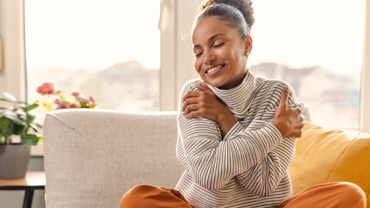 Woman on couch hugging herself and smiling | Start the New Year Right with a Quick Mental Health Check-In | Mindful Health Solutions