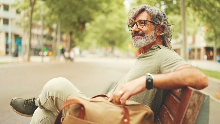 Older man siting on a bench in a city smiling | Are You Suffering from Chronic Pain? Find Hope with TMS | Mindful Health Solutions