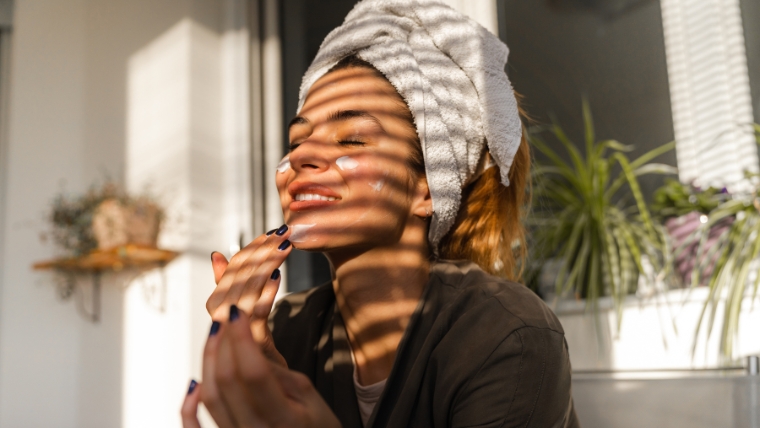 Woman with a towel around her hair applying face cream | How To Build Healthy Habits and Embrace Self-Care in the New Year | Mindful Health Solutions