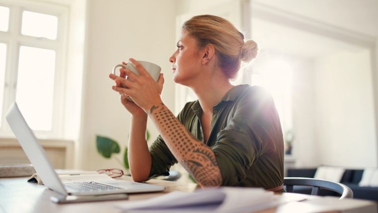 A person sitting at a table with a laptop and a cup of coffee looking thoughtfully out the window | Is Accelerated TMS Safe 5 Potential Side Effects to Make Informed Decisions | Mindful Health Solutions