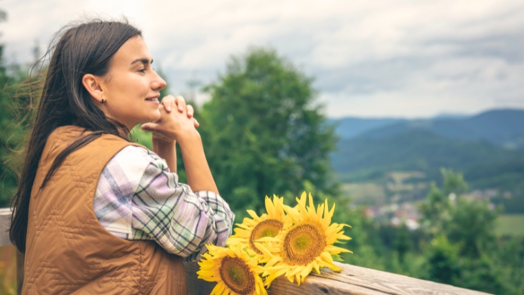 Young woman looking at sunflowers on a wooden deck | Self-Love: How To Grow a Strong and Loving Relationship with Yourself | Mindful Health Solutions