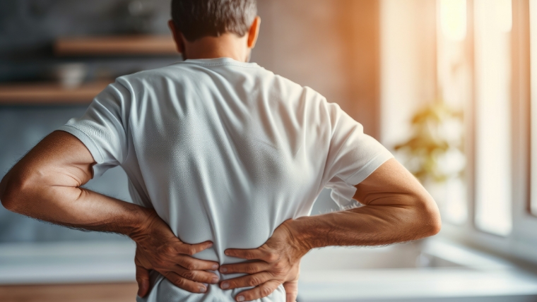 A mature man standing in his kitchen with his hands holding his back | How Your Chronic Pain and Mental Health Go Hand-in-Hand | Mindful Health Solutions