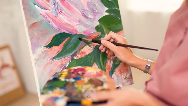 A woman's hand holding a paint palette and painting a flower on a canvas | 9 Amazing Therapeutic Benefits of Art for Anxiety Management | Mindful Health Solutions